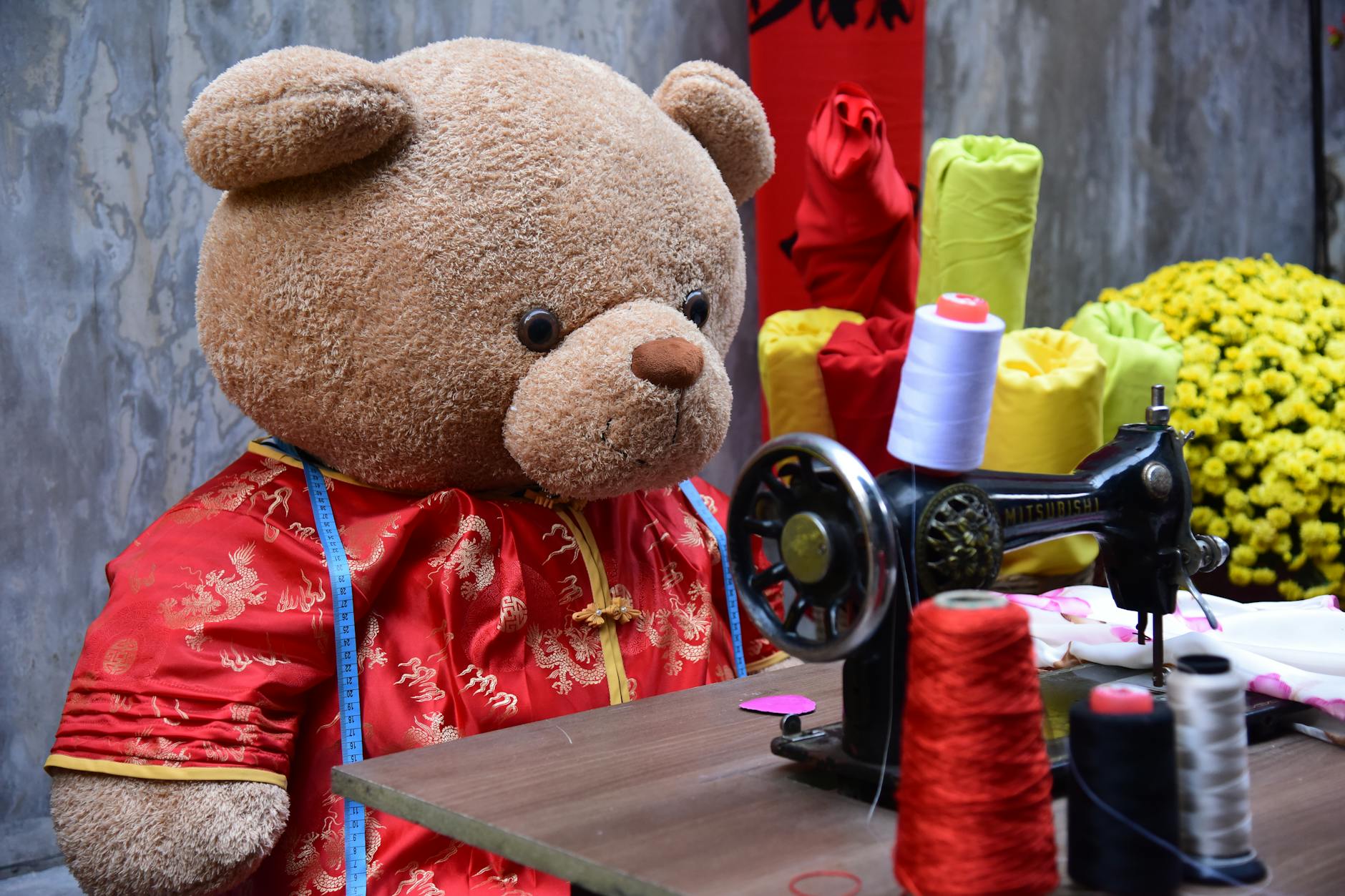 Pluszowy miś przy maszynie do szycia szyjący czerwoną tkaninę