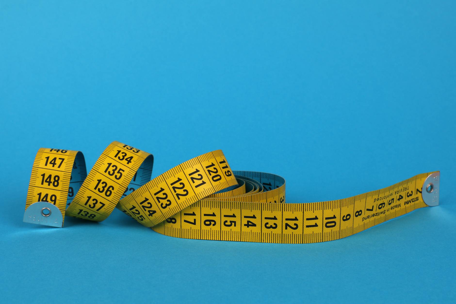 Żółta miarka krawiecka zwinięta na niebieskim tle