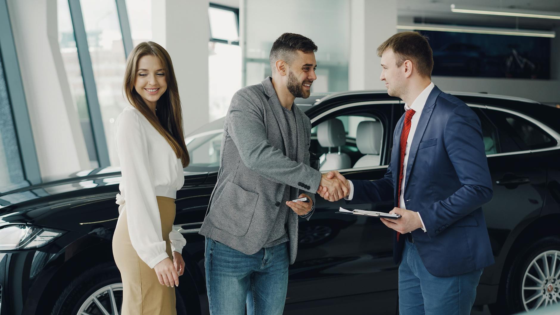Klient i sprzedawca ściskają sobie dłonie w salonie samochodowym