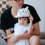 Tata przytula córkę w czapce z uszami misia w przytulnym wnętrzu