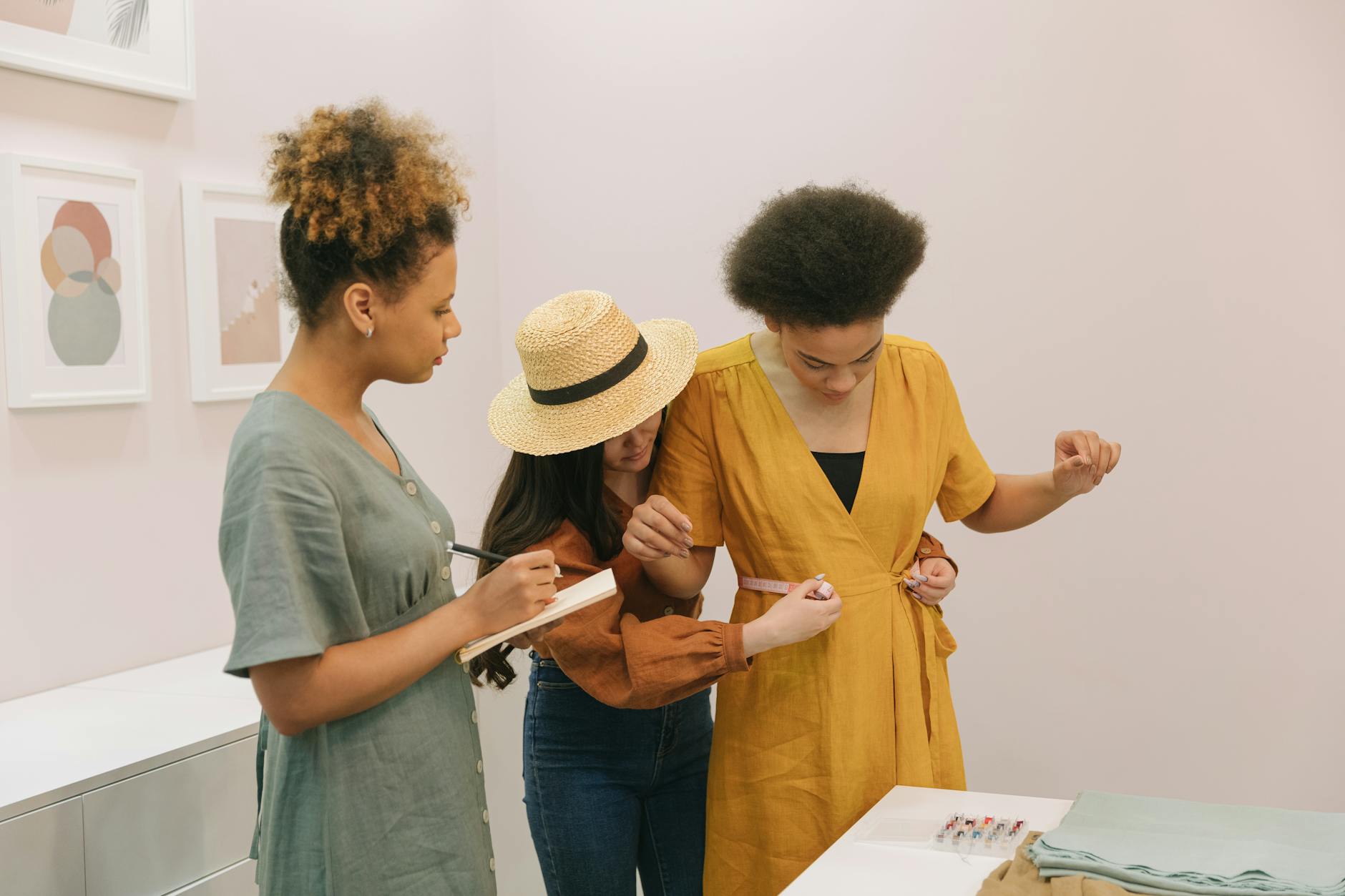 Trzy kobiety mierzą ubranie w pracowni krawieckiej